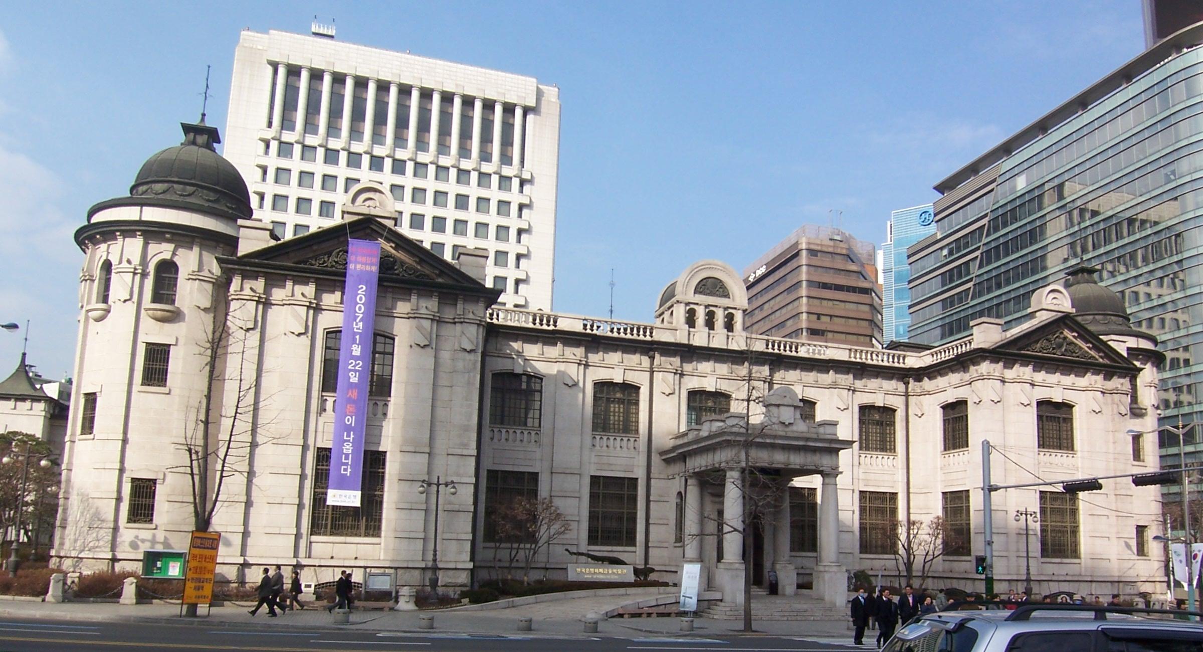 Tòa nhà đá lịch sử của Ngân hàng Hàn Quốc tại Seoul, với các tòa nhà cao tầng phía sau.